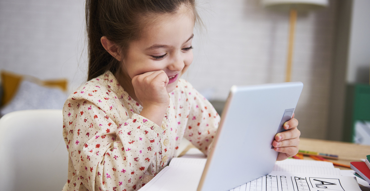 girl using a tablet while completing a worksheet on the alphabet